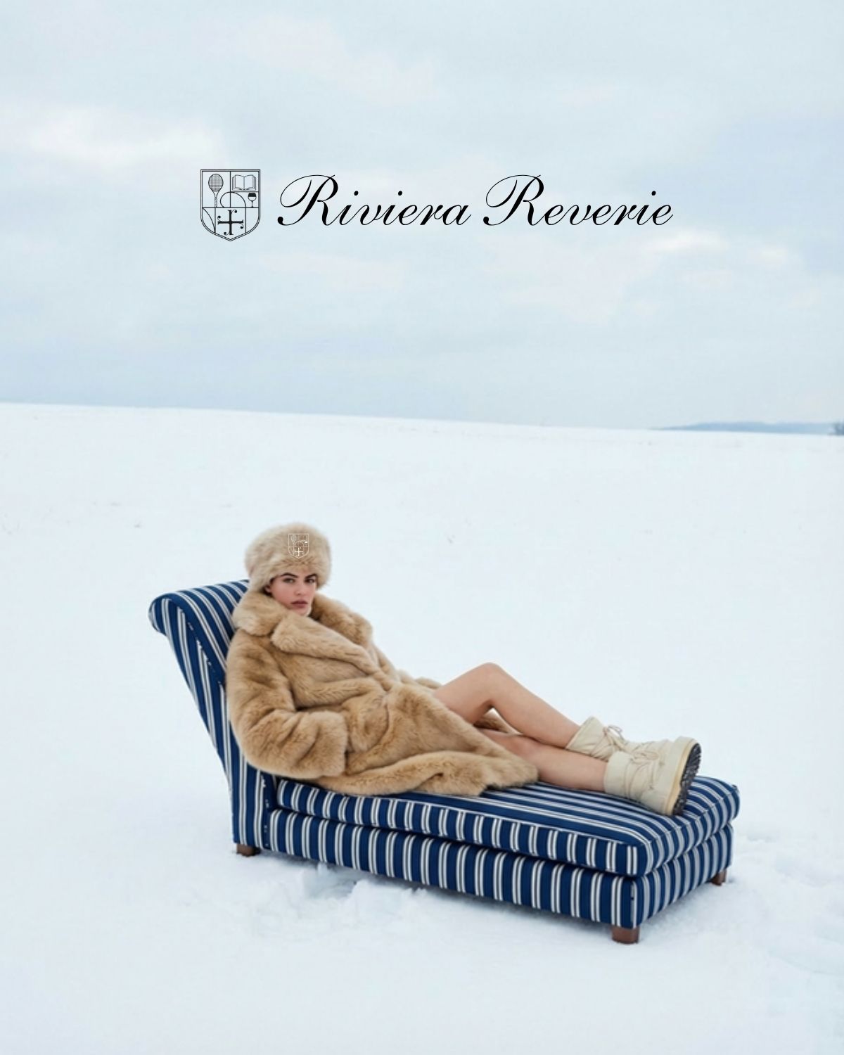 A woman in a camel coat on a navy striped chaise in the snow