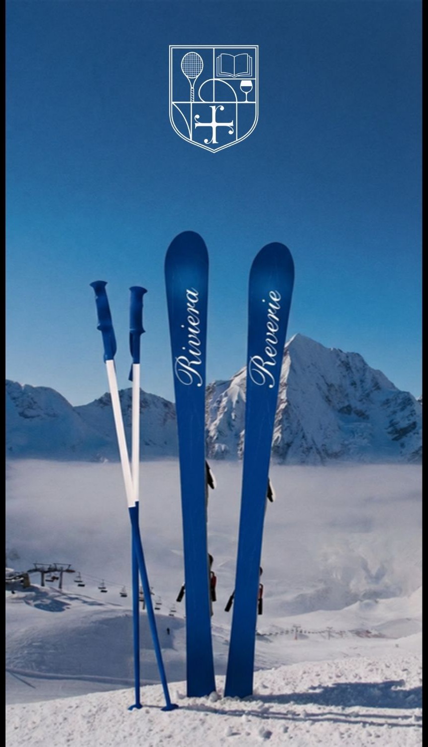 Navy skis with the Riviera Reverie script standing in snow above the clouds